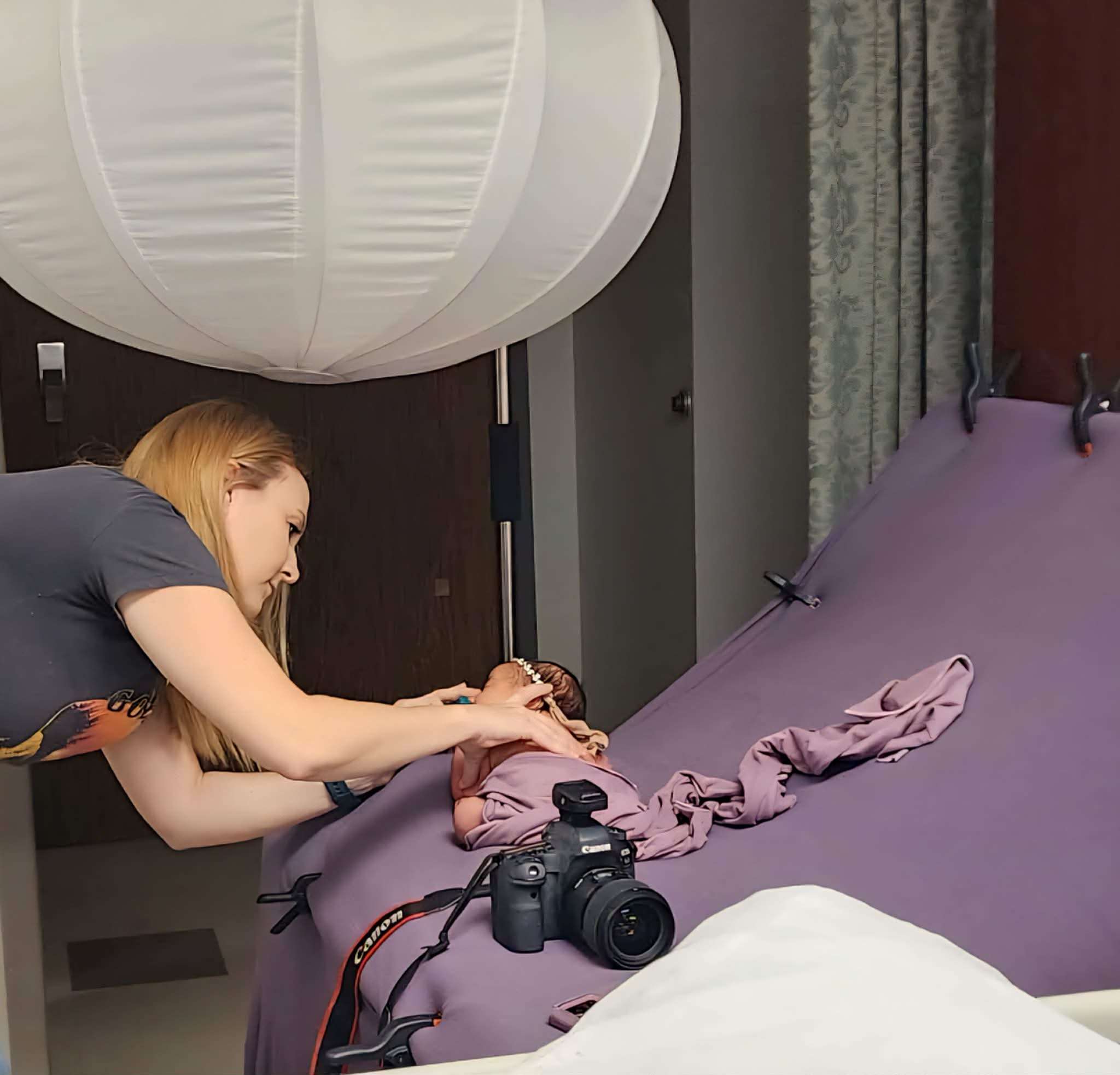 Photographer carefully posing a newborn baby on a purple backdrop in a hospital room