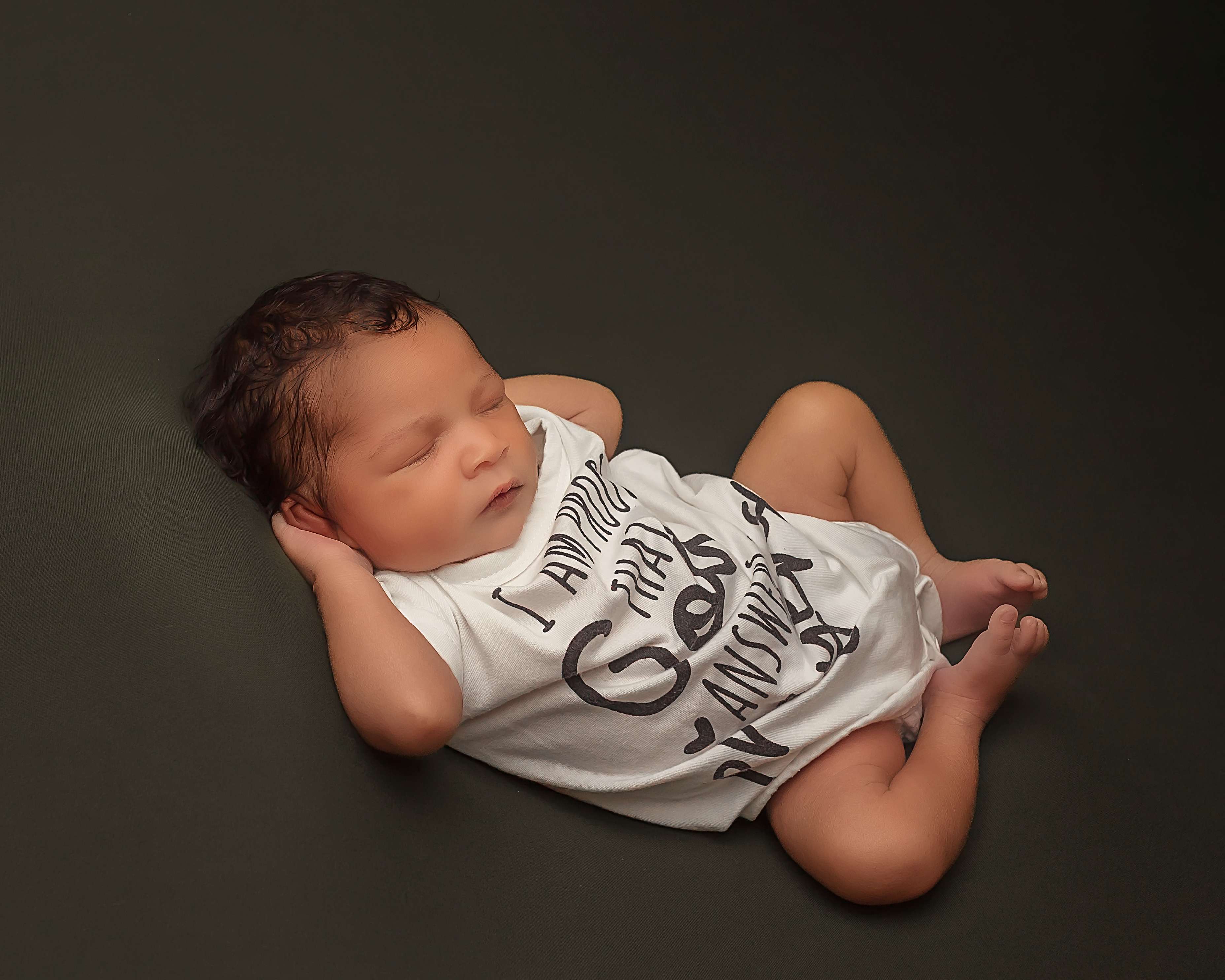 Newborn baby boy sleeping in a white printed onesie on a dark backdrop