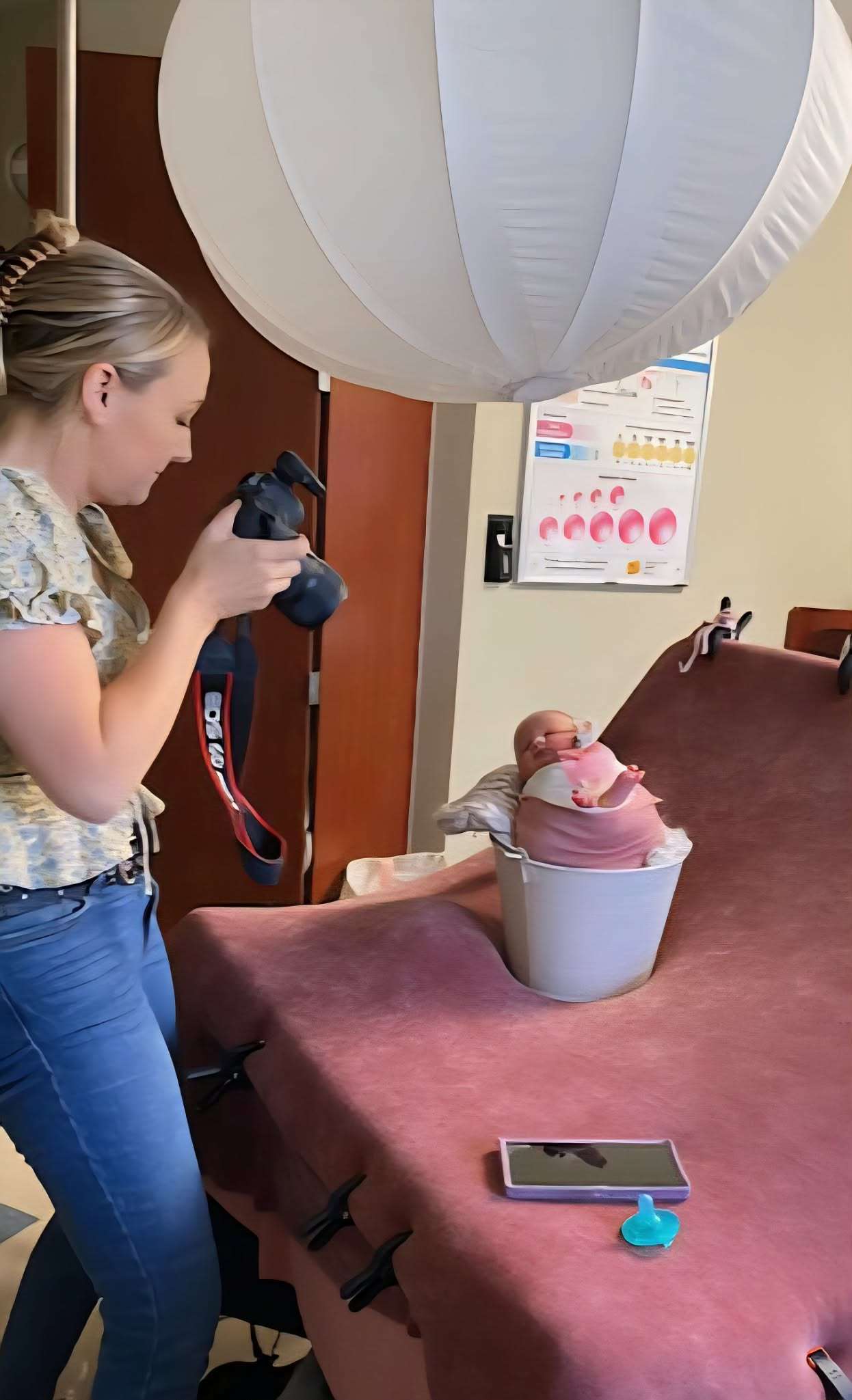 Photographer photographing a wrapped newborn in a bucket on a posing table inside a hospital room